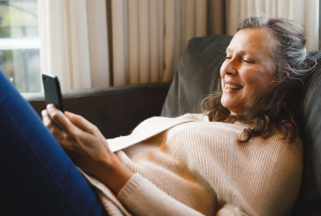 Happy senior woman in living room sitting on couch talking on phone.
