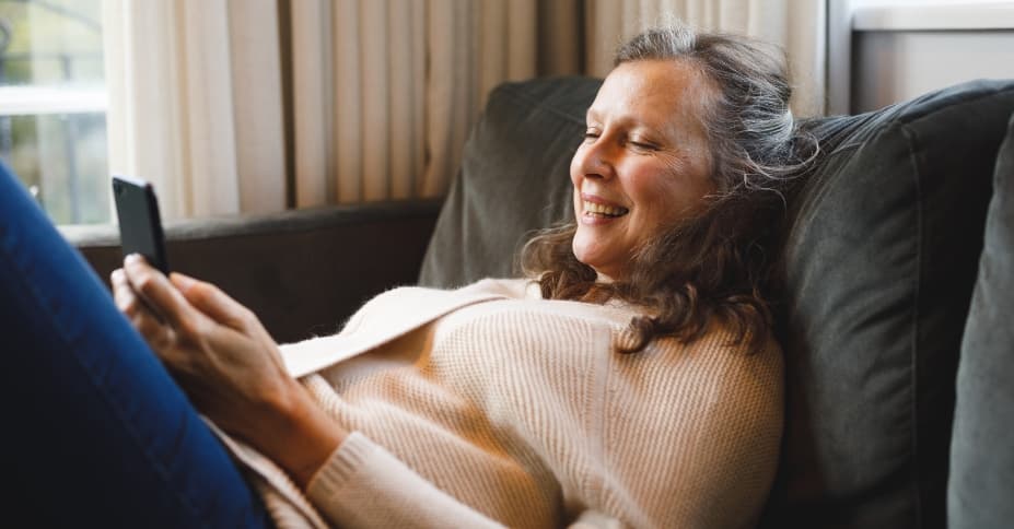 Happy woman using smart phone on couch.