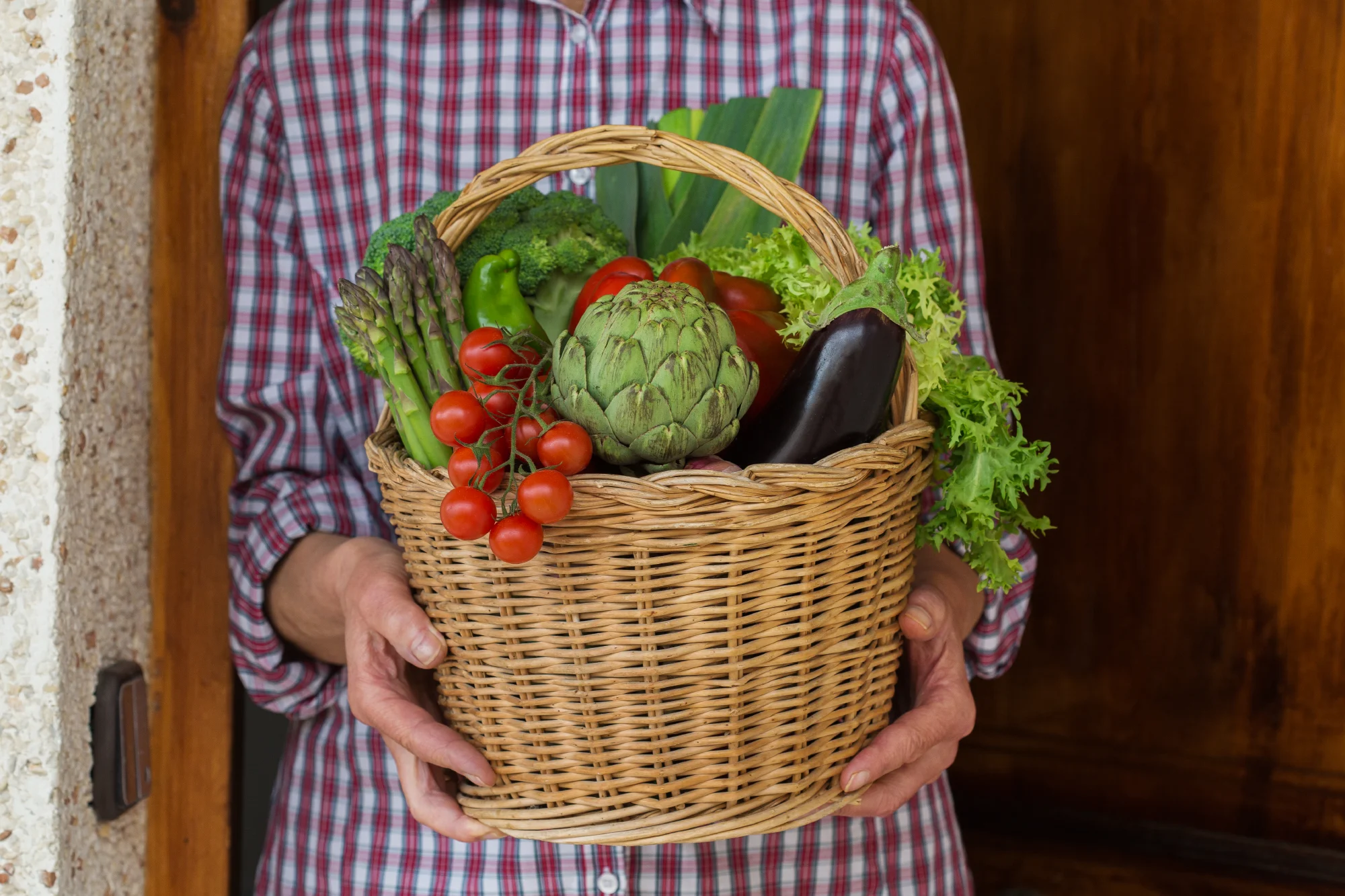 Woman holding a basket full of an assortment of organic farmer produced vegetables.