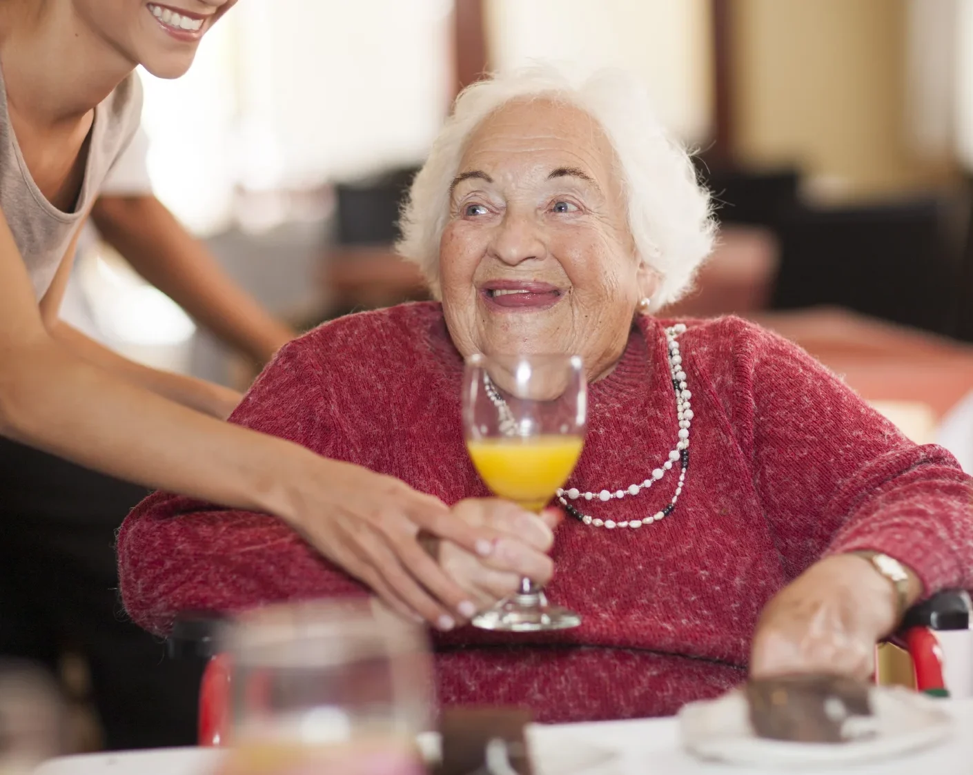 Caregiver assisting senior woman with drinking her orange juice