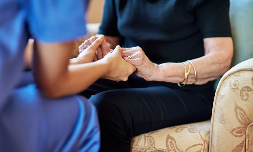 Empathetic caregiver holding hands with senior woman while they talk.